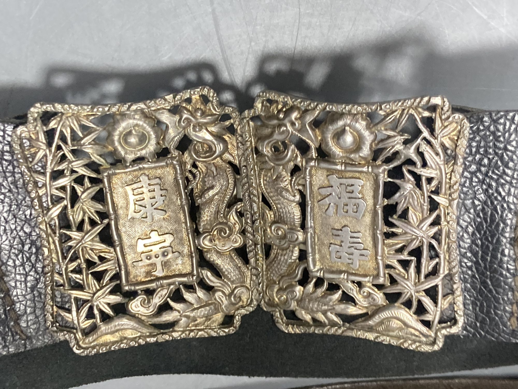 A Chinese white metal cigarette case by Luen Hing, 75mm and four pairs of Chinese white metal belt buckles, three mounted on leather